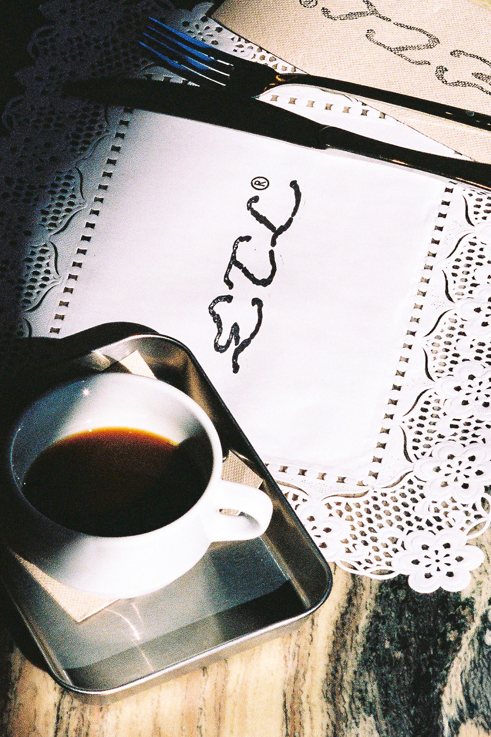 Wordmark printed on a paper doily next to a cup of espresso, soft daylight.